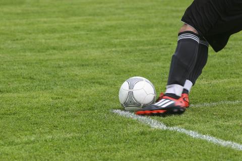 Person kicking soccer ball on soccer field. 